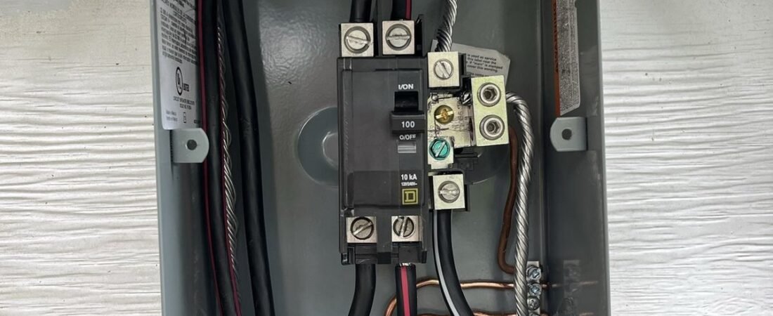Open outdoor electrical service panel with a 100-amp main breaker, wiring and grounding lugs mounted on white siding